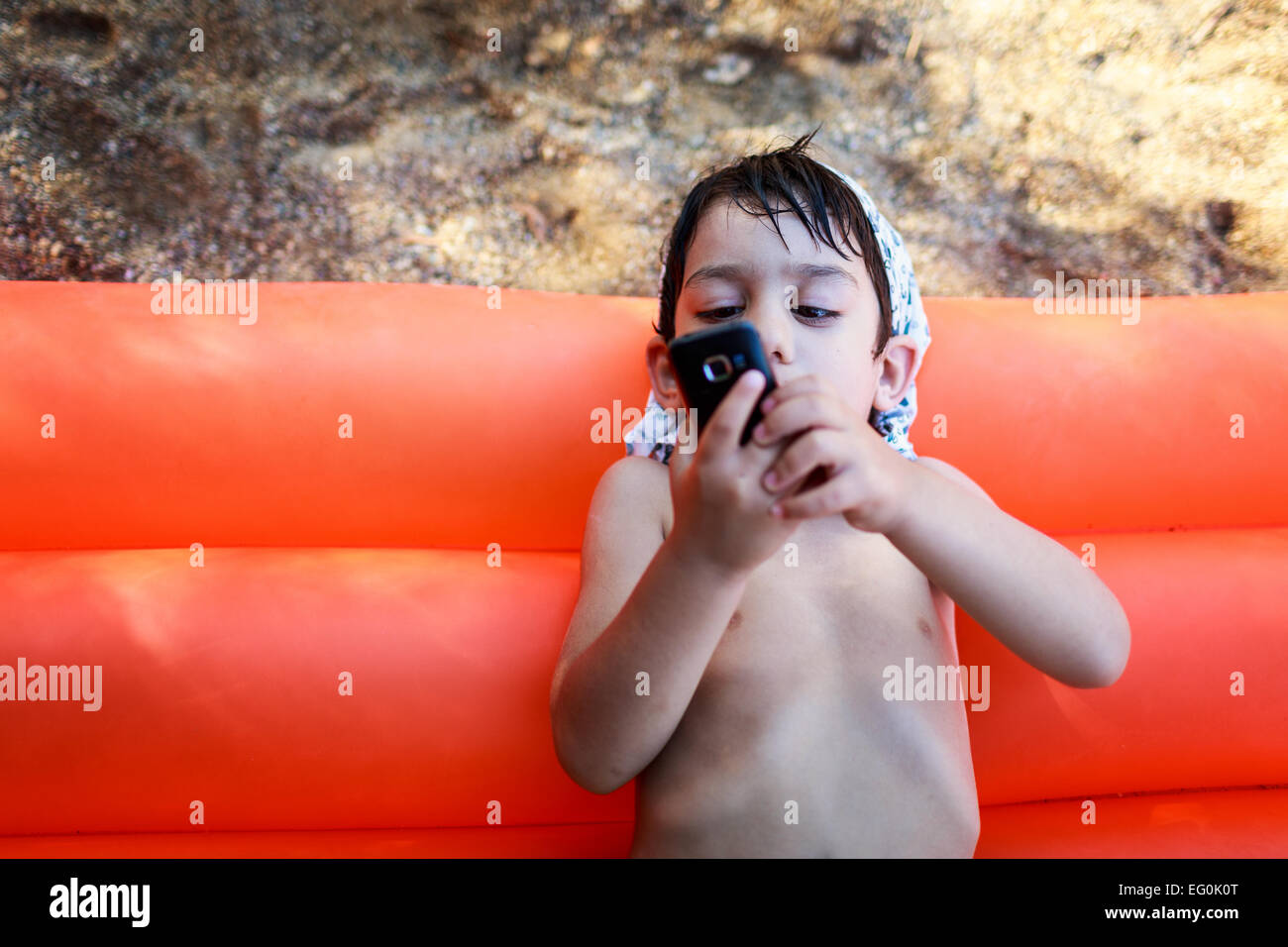 La Bulgaria, Sofia, ragazzo (4-5) giacente sul rosso zattera pool utilizzando il telefono cellulare Foto Stock