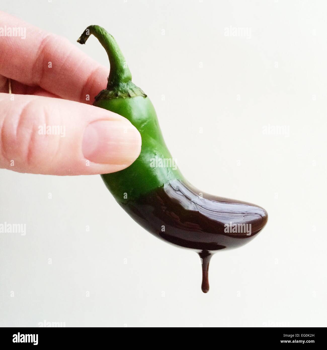 Mano umana con un pepe Jalapeno immerso in salsa di cioccolato caldo Foto Stock