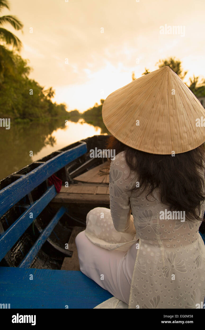 Donna che indossa ao dai vestito in barca all'alba, Can Tho, Delta del Mekong, Vietnam Foto Stock