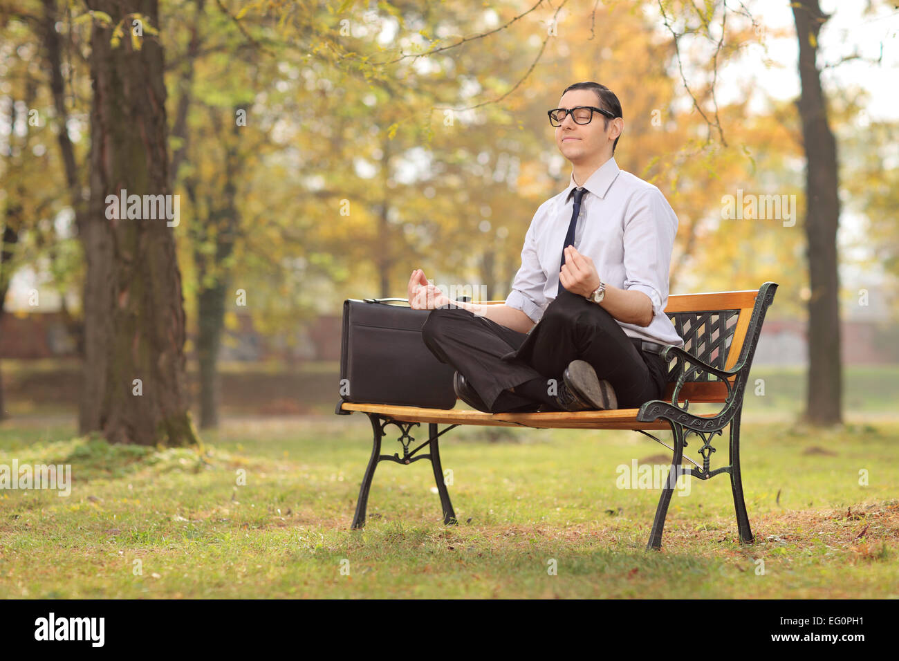 Imprenditore rilassato meditando seduto su una panchina nel parco Foto Stock