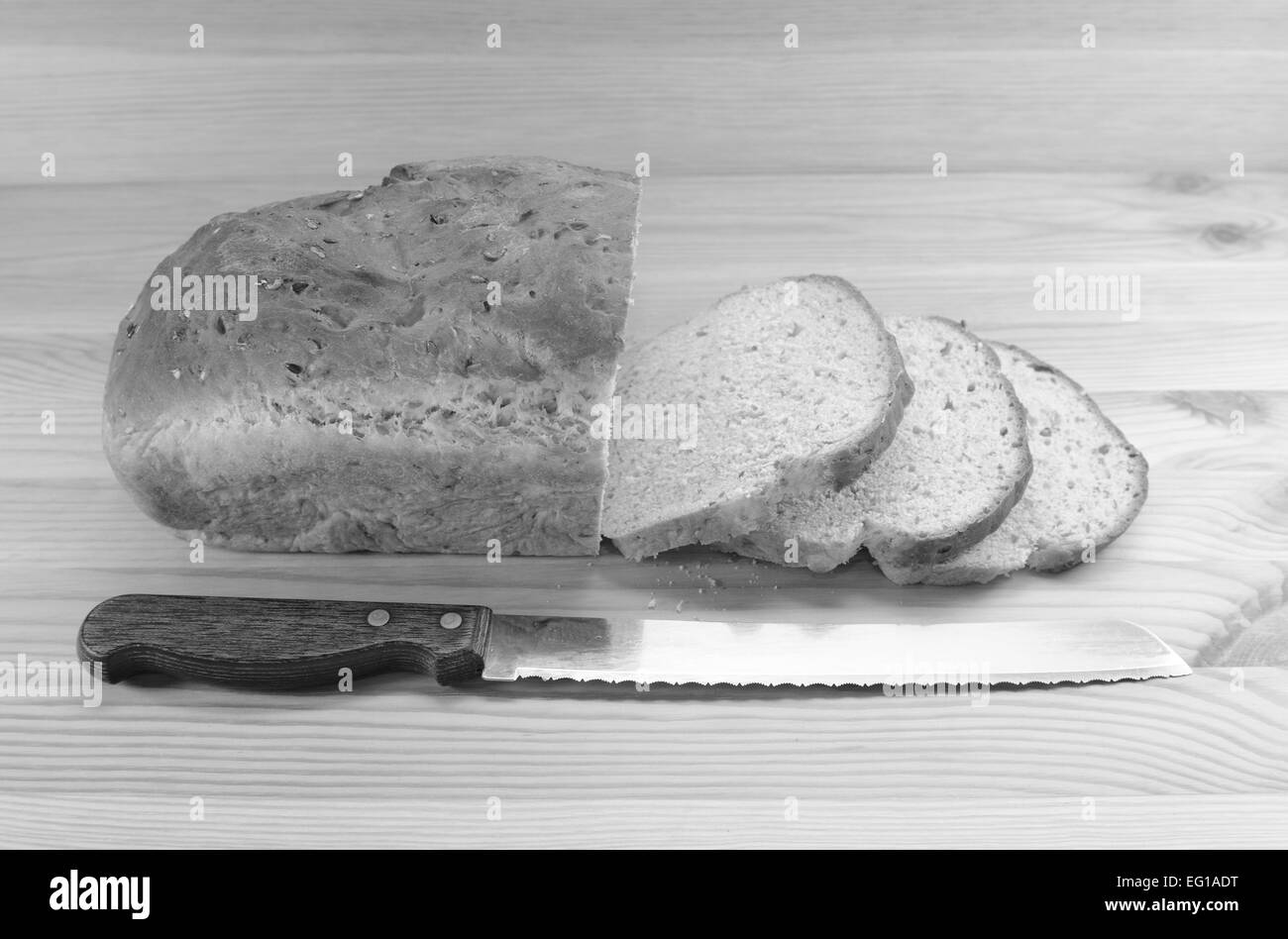 Tre fette tagliate da una pagnotta di pane con un coltello sul tavolo di legno - elaborazione monocromatica Foto Stock