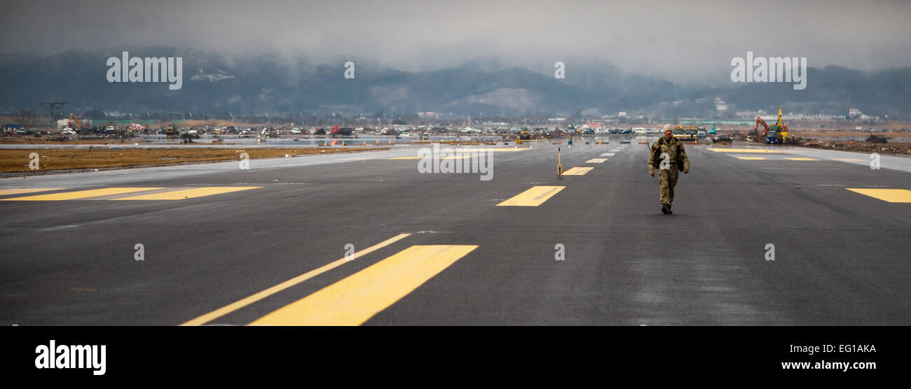 Un controllore di combattimento cammina giù per la pista principale all'Aeroporto di Sendai, misurando l'area utilizzabile per vedere se un C-130 può atterrare vi Marzo 16. Il personale Sgt. Samuel Morse Foto Stock