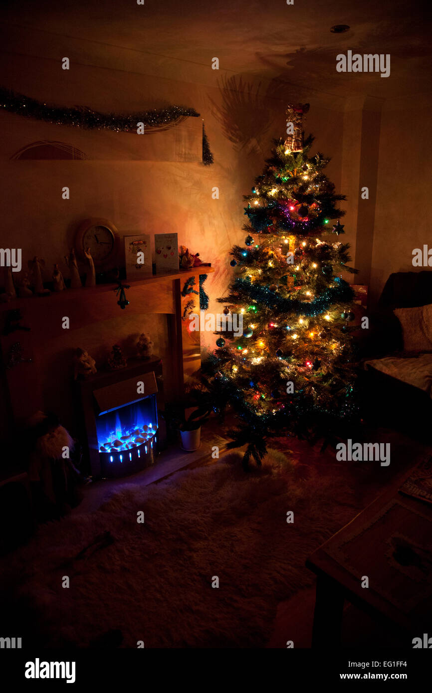 Albero di Natale decorato con luci di posizione accese, in una stanza buia con blu di fiamma di fuoco di effetto Foto Stock