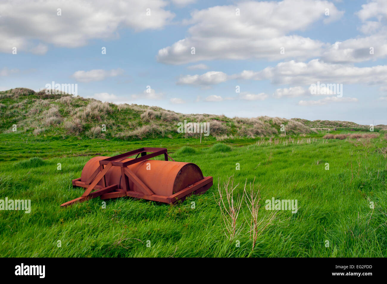 Verde e lussureggiante campo sulla costa con un agricoli abbandonati rullo pesante Foto Stock