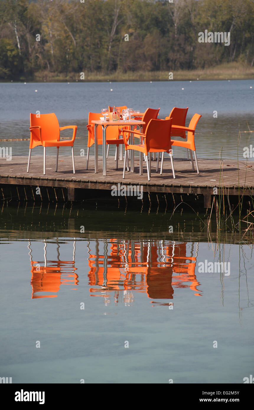 Orange tavolo e sedie si riflette nel lago di Banyoles situato in Pla de l'Estany, provincia di Girona, in Catalogna, Spagna Foto Stock