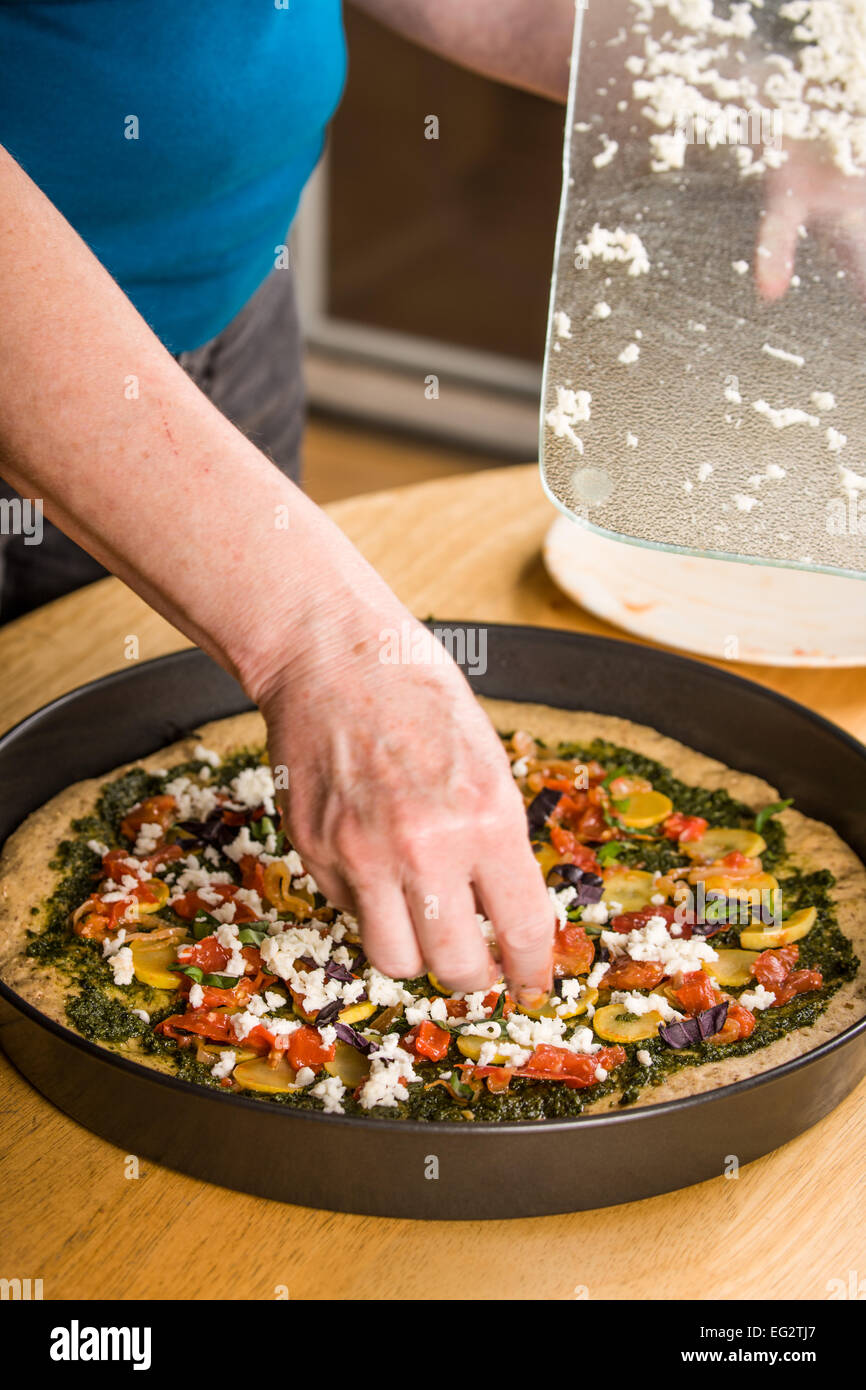 Donna di irrorazione, grattugiato mozzarella fresca su un vegetariano, multi-granella spessa crosta di pizza Foto Stock