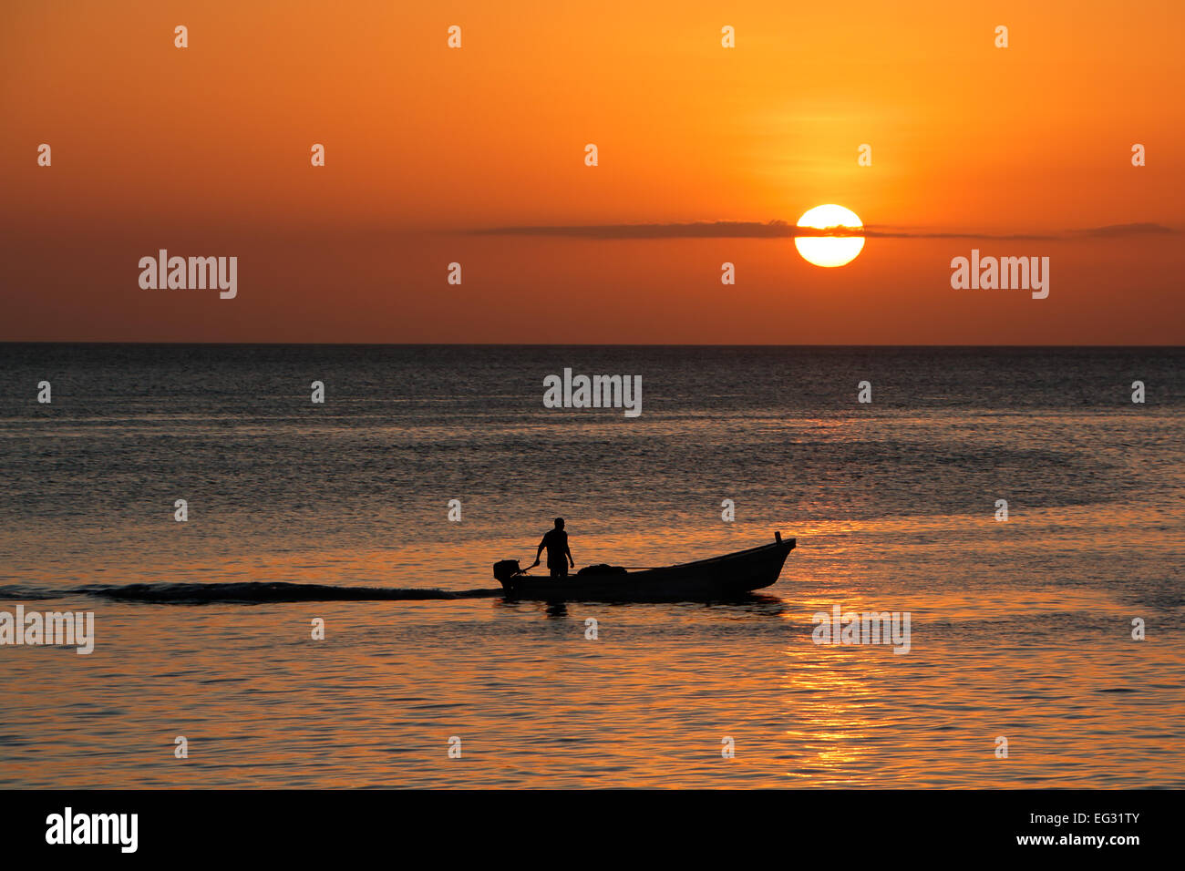 Silhouette di una piccola barca contro un tramonto dorato, isola di Zanzibar Foto Stock