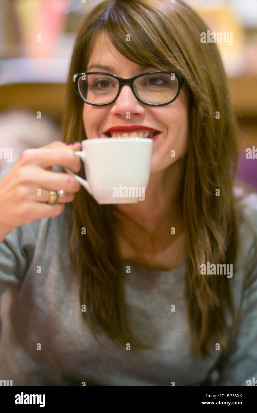 Bella giovane donna gustando una bevanda calda con gli amici in una accogliente caffetteria. Foto Stock