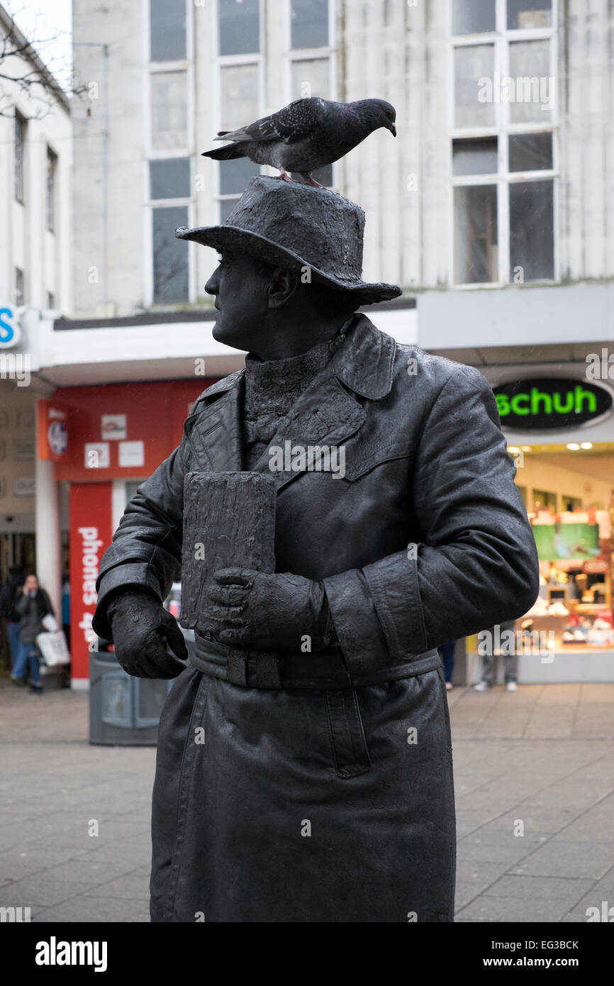 L'uomo tutti in abiti neri e oscurati la faccia di posa come una statua con un piccione sulla sua testa nella trafficata città di Portsmouth Inghilterra centrale Foto Stock