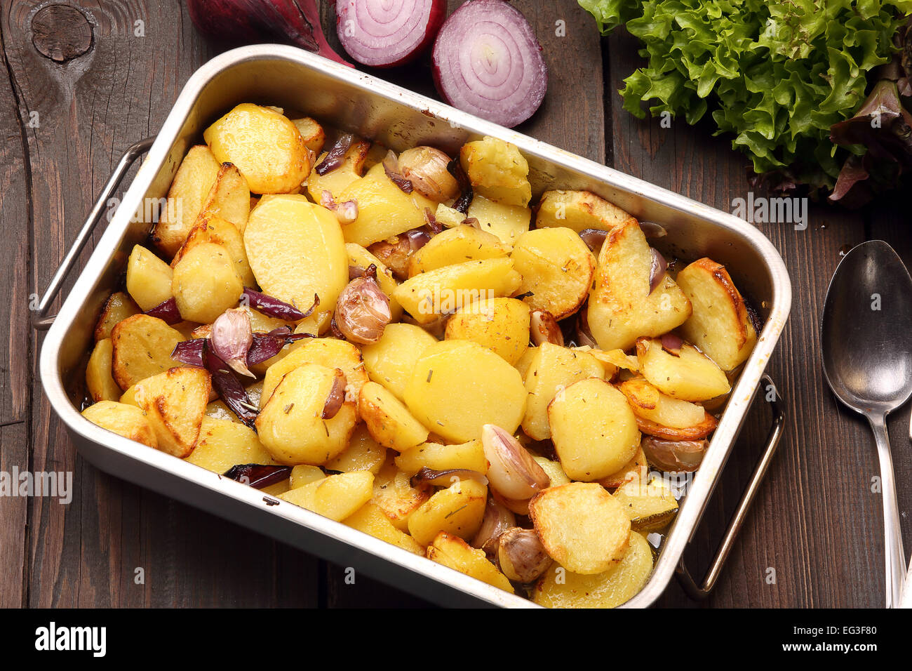 Patate al forno in una teglia con aglio e cipolla su un sfondo di legno  Foto stock - Alamy