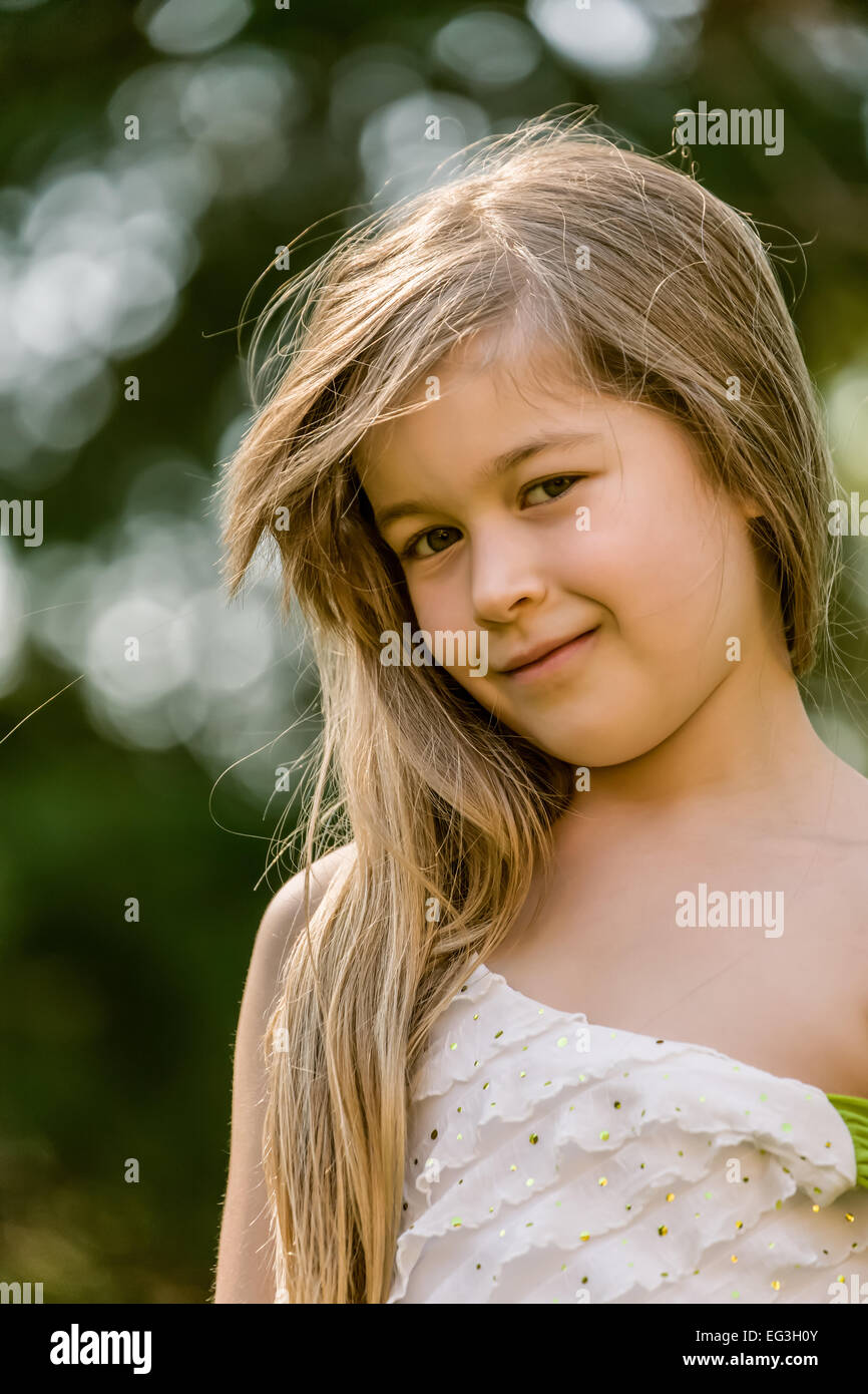 Ritratto di sette anni, con i capelli lunghi bambina indossa un abito senza maniche esterno, guardando molto coy e dolce Foto Stock