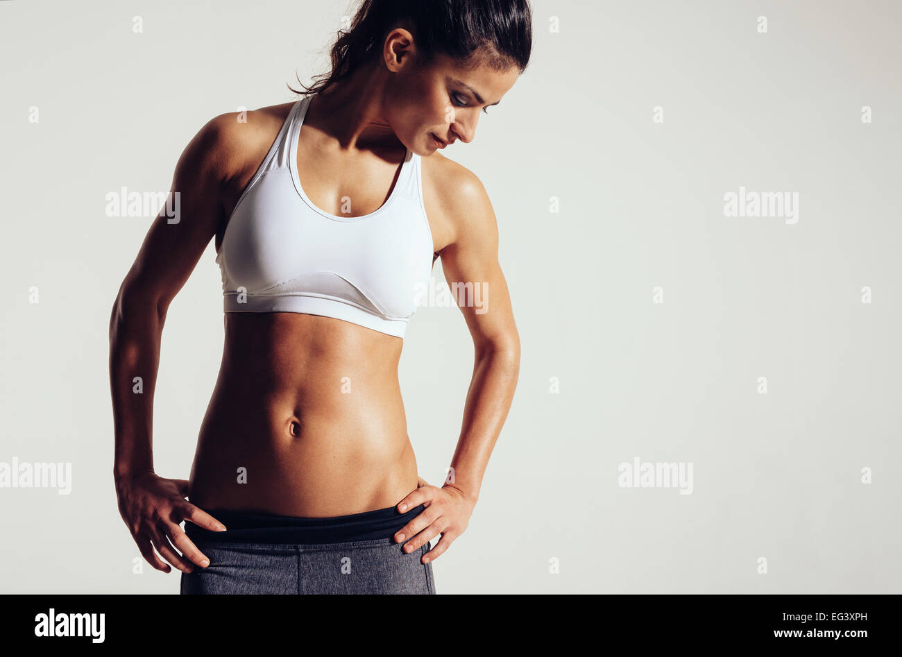 Attraente giovane donna in abbigliamento sportivo in posa su uno sfondo grigio. Sottile e un sano modello femminile in studio. Foto Stock