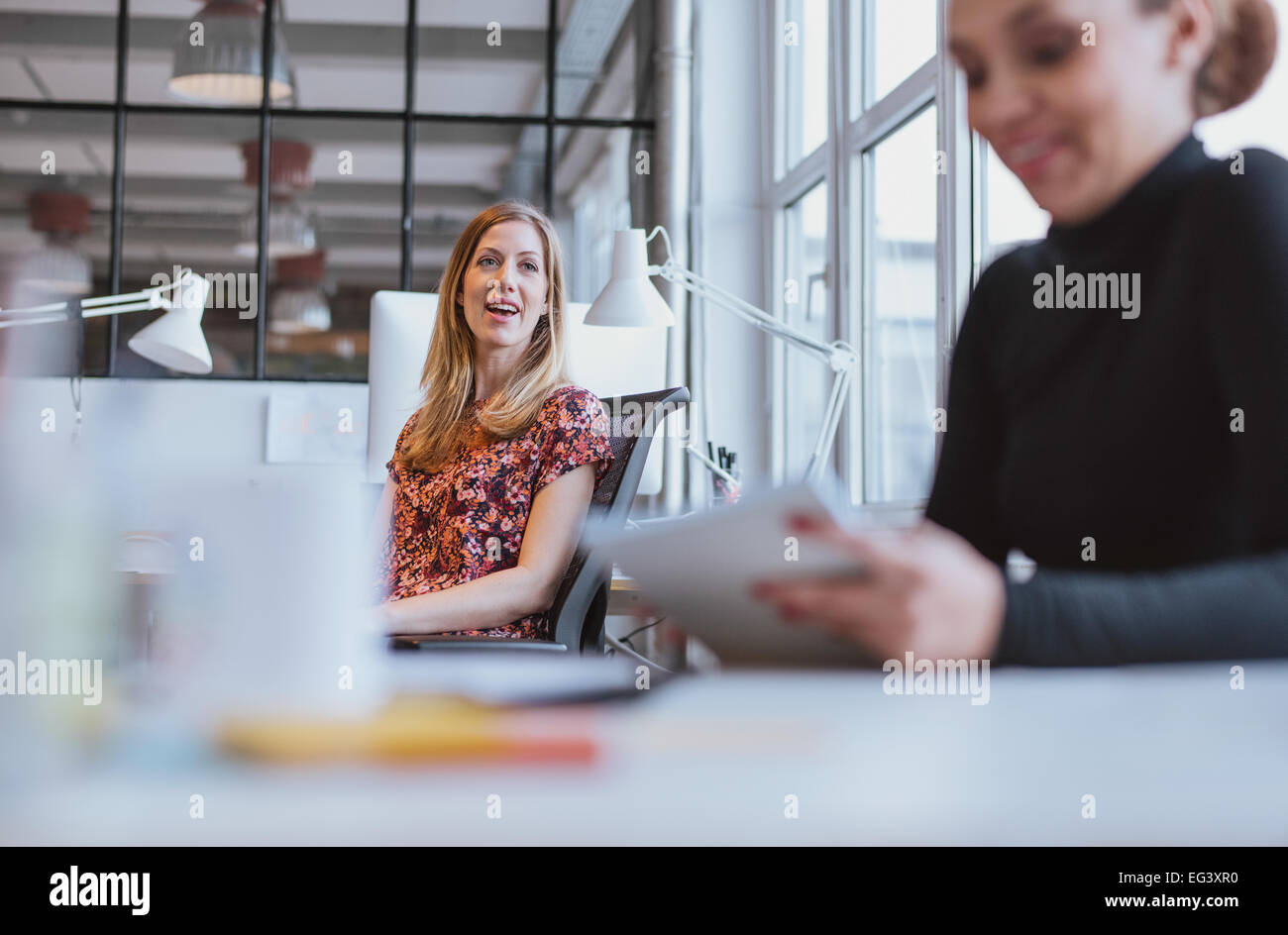 Felice giovane donna avente una conversazione amichevole con il suo collega di sesso femminile mentre si è al lavoro Foto Stock