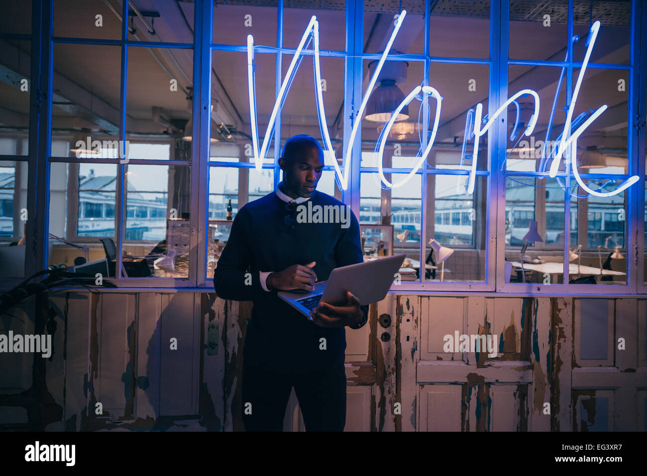 I giovani africani man standing in ufficio utilizzando il computer portatile. Business executive in ufficio con grande luce al neon segno di lavoro. Foto Stock