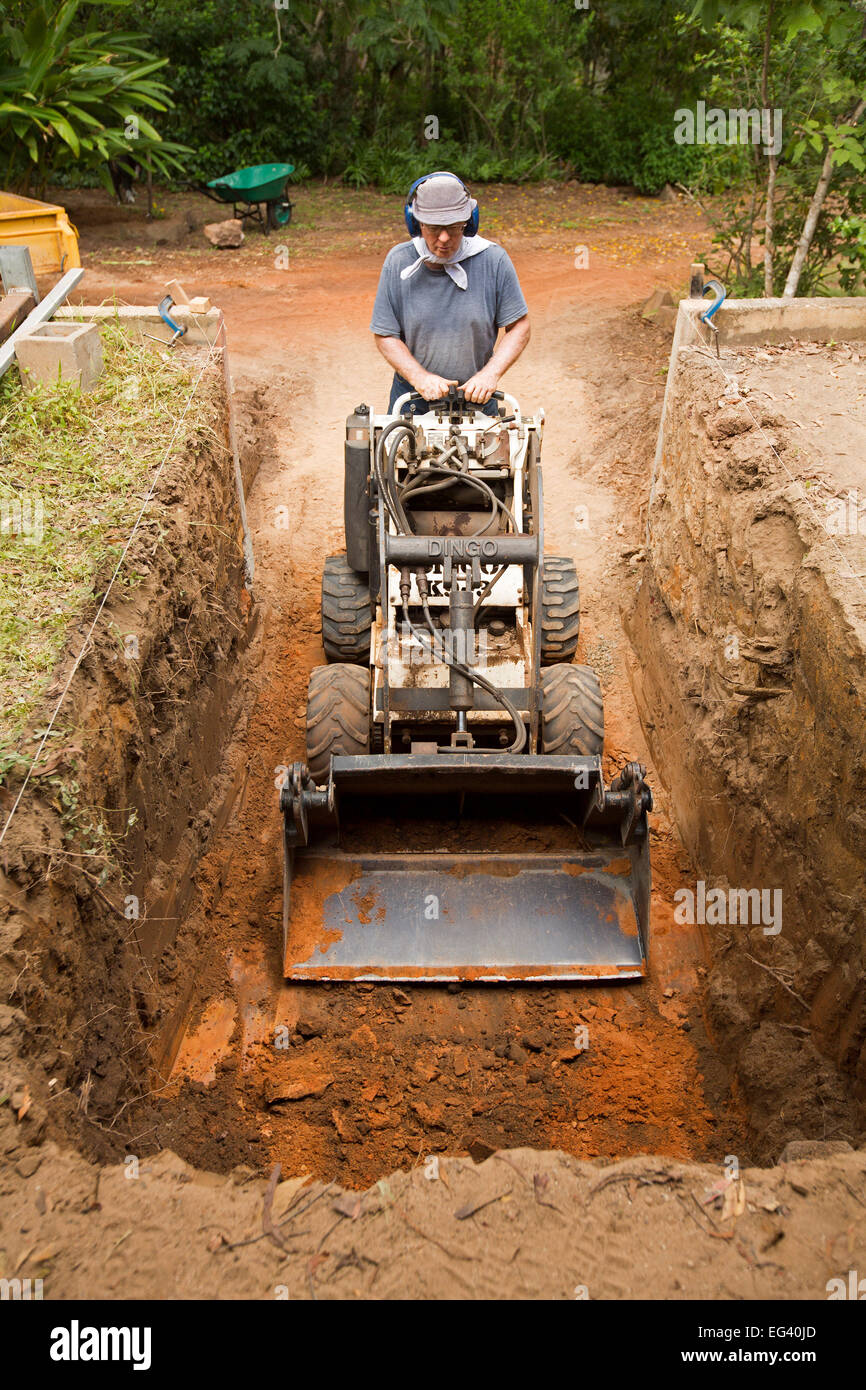 Uomo di funzionamento / escavatore macchina movimento terra sul sito di costruzione con la macchina all'interno di profonda trincea larga Foto Stock