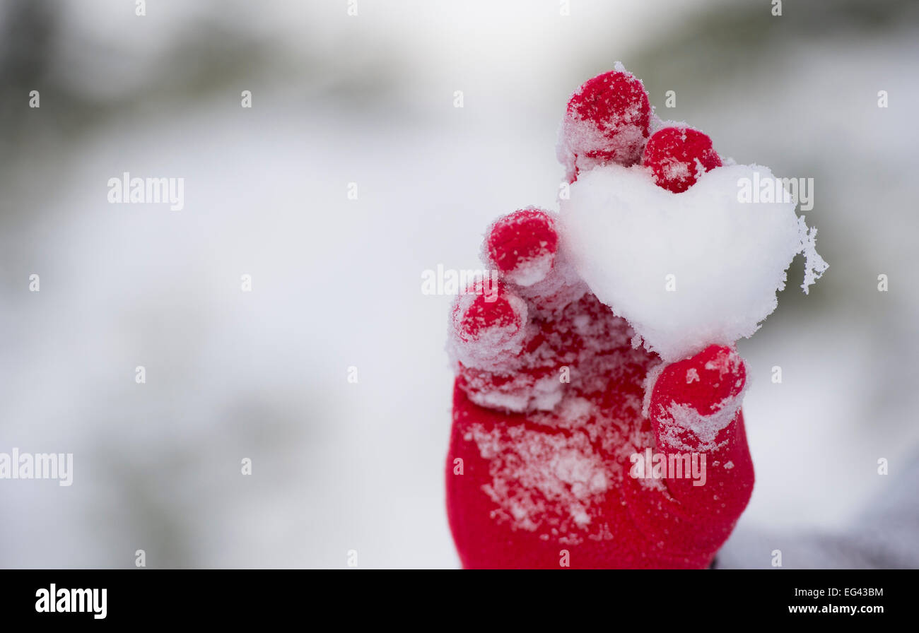 Guanti rossi tenendo un cuore fatto da neve Foto Stock