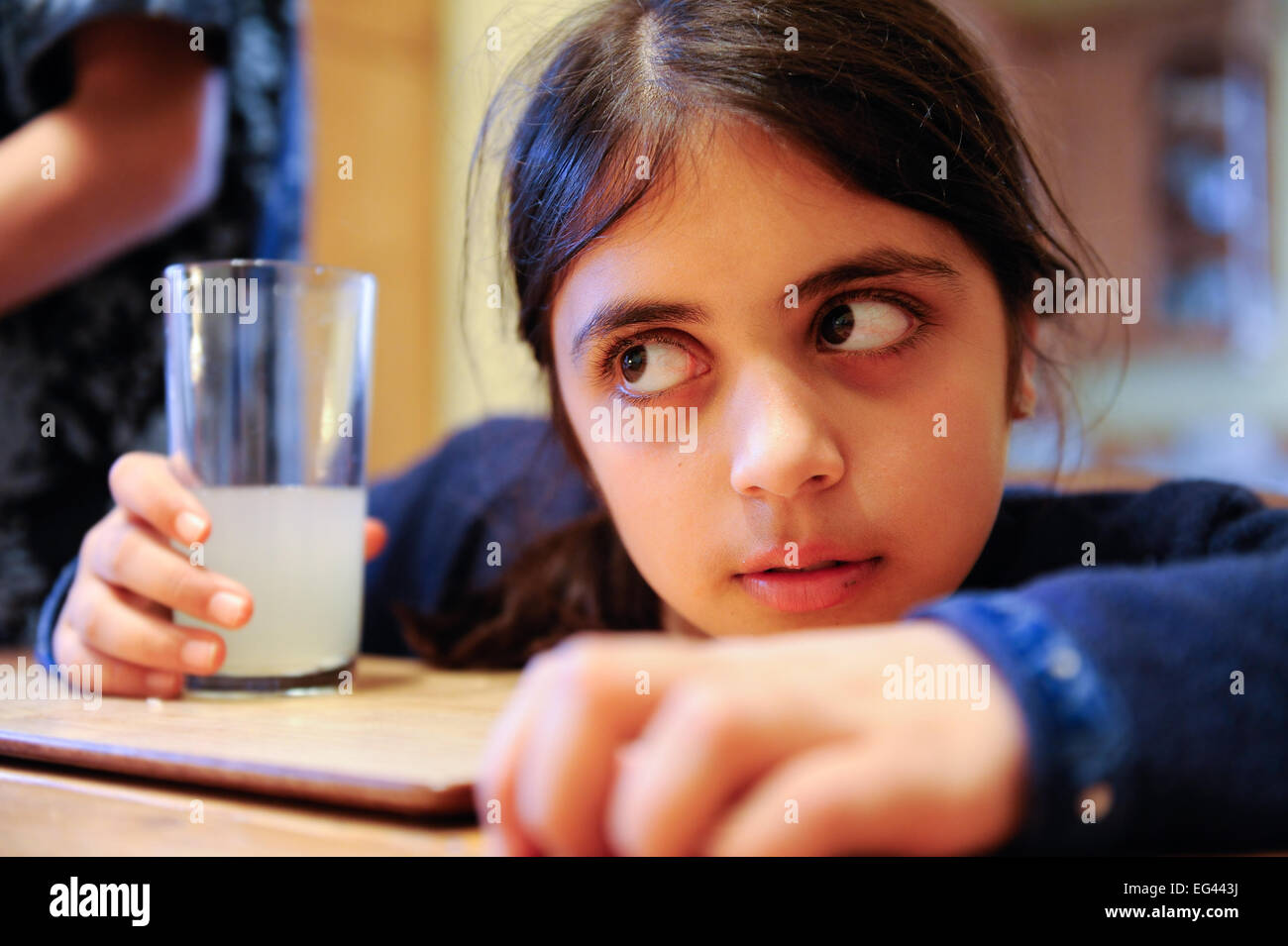 Giovane ragazza con un bicchiere di limonata in un vetro pensa profondamente su quello che sta succedendo altrove attraverso la tabella Foto Stock