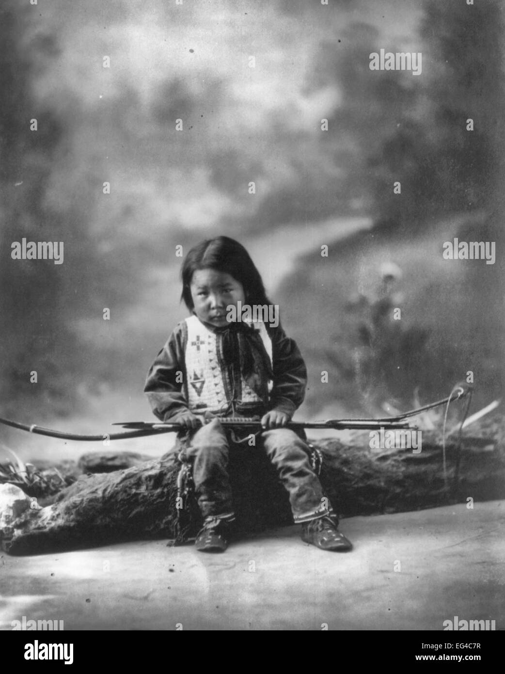 John Lone Bull - a lunghezza piena, seduto su log, una gamba nascosto sotto le altre, rivolto verso sinistra. Sioux bambino indiano, circa 1900 Foto Stock