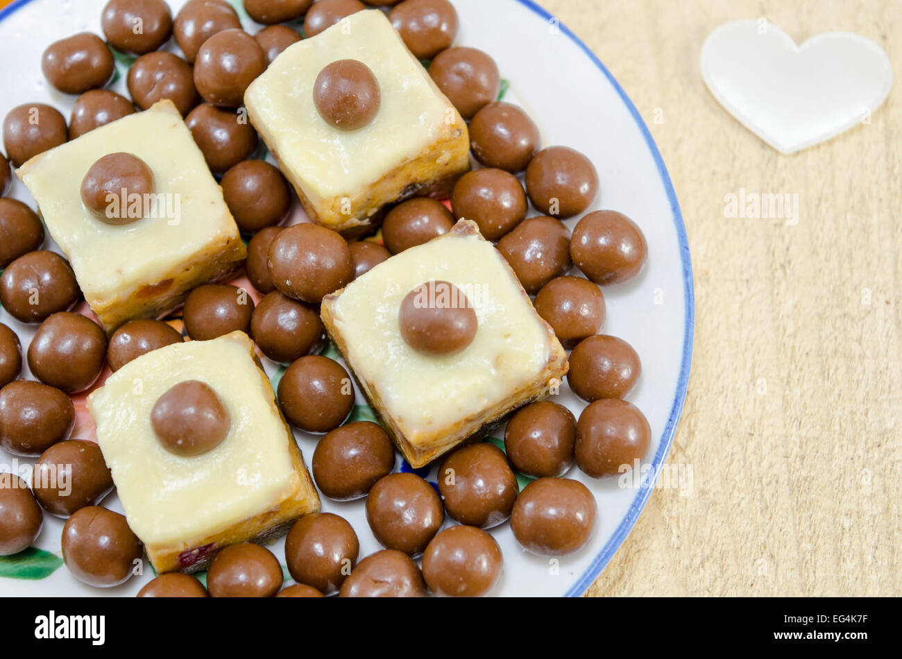 Dolci fatti in casa in una lastra decorata con palline di cioccolato e un bianco seta cuore sul tavolo Foto Stock