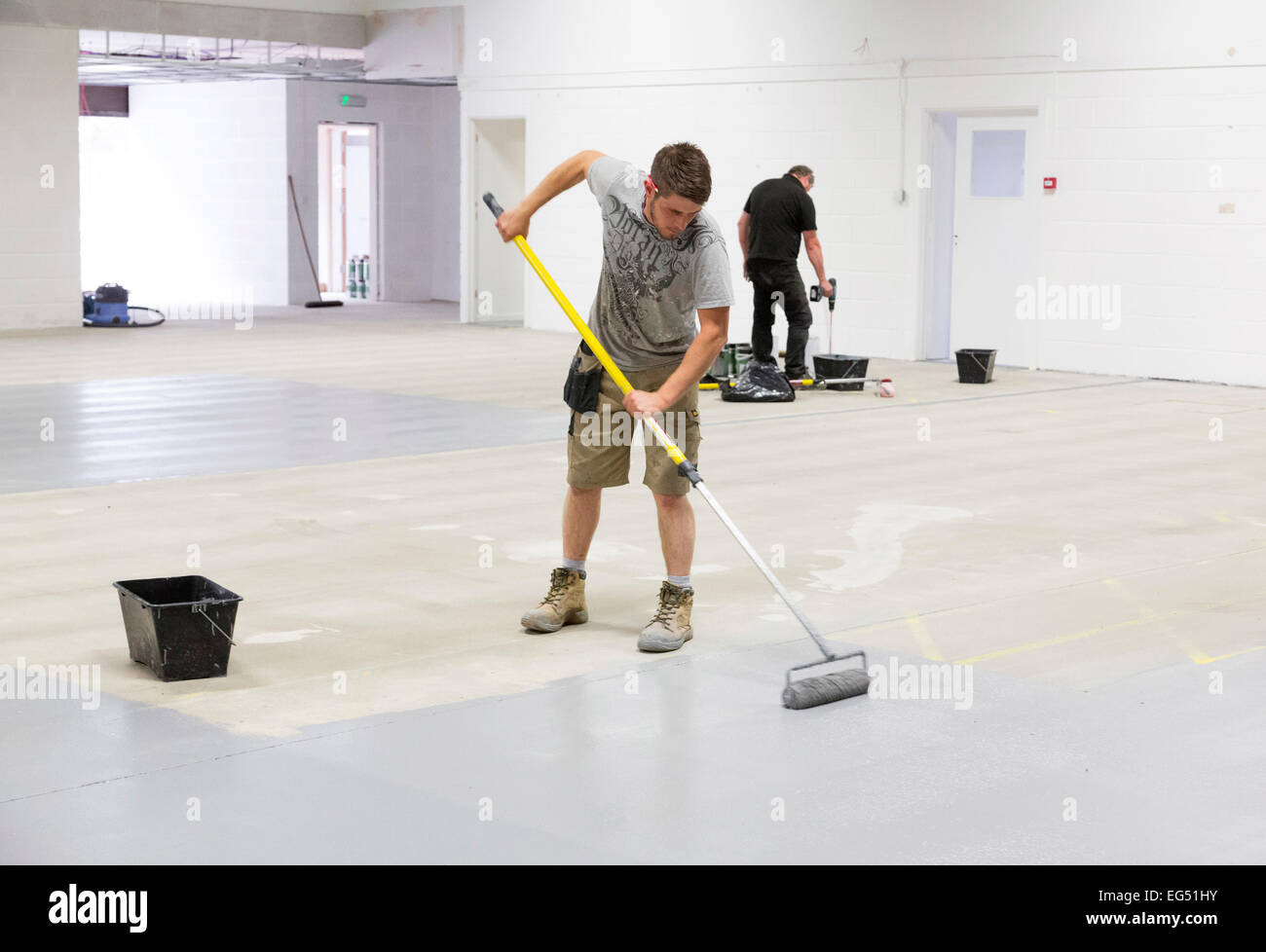 Un lavoratore dipinto il pavimento di una fabbrica con base epossidica vernice per hard durata Foto Stock