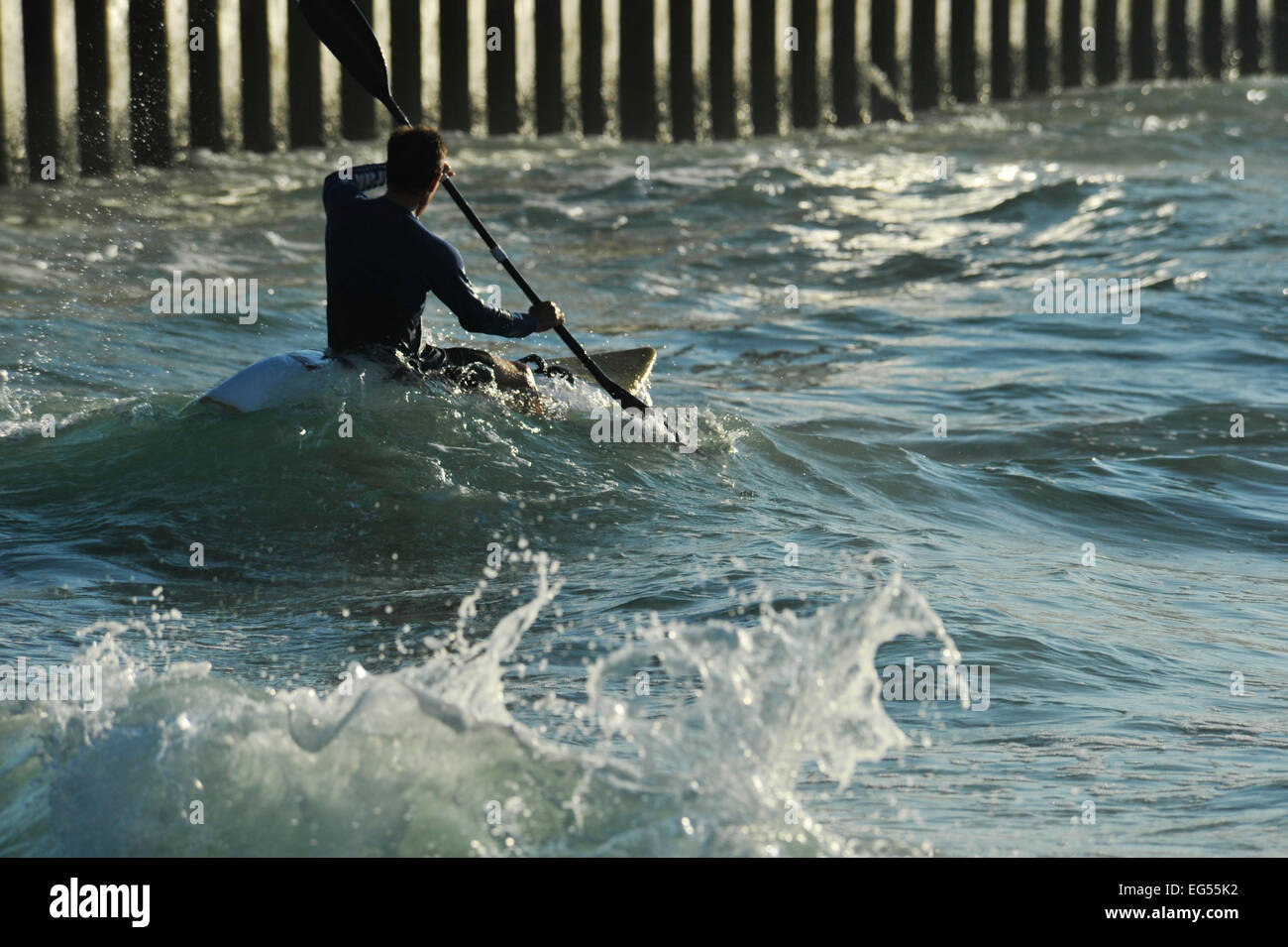 Durban, KwaZulu-Natal, Sud Africa, silhouette, singolo uomo adulto canoa kayak di mare, turbolento onde, pilastri del molo, persone, spiaggia Foto Stock