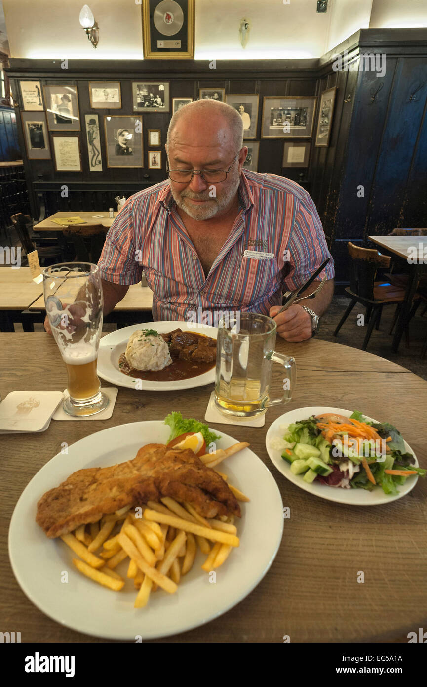 Uomo anziano seduto davanti a un pasto abbondante, in corrispondenza della parte anteriore di una piastra di schnitzel e chip in un ristorante bavarese, Monaco di Baviera Foto Stock