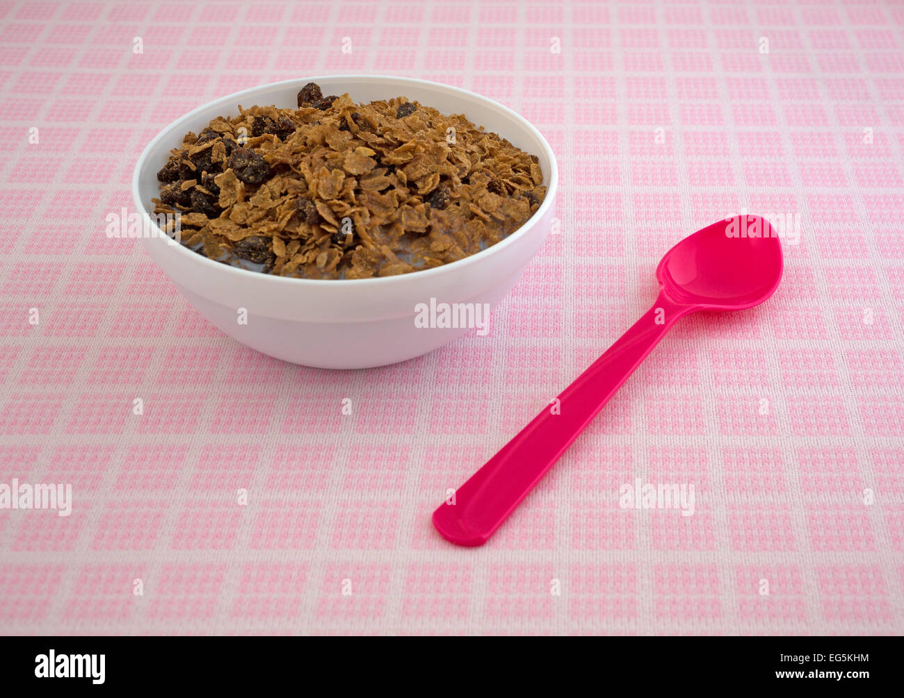 Una ciotola di grano intero uvetta su una tovaglia con un cucchiaio di rosa a lato. Foto Stock