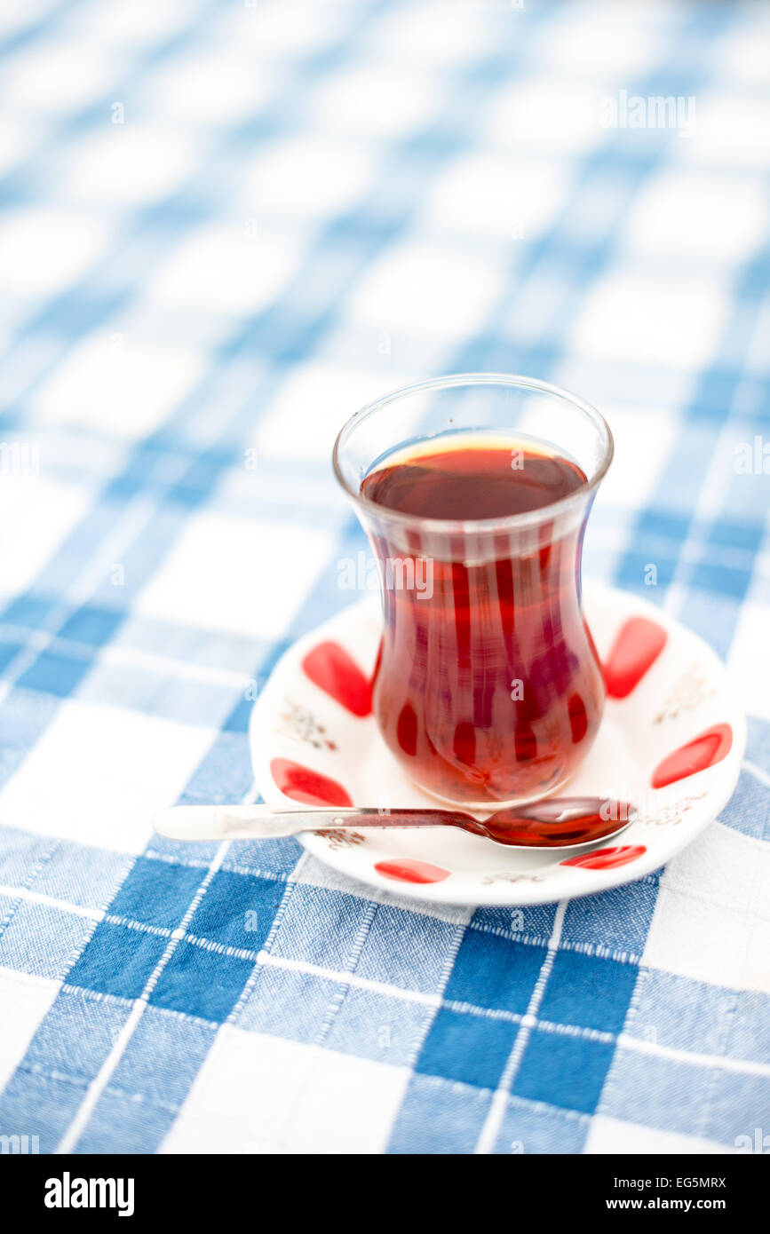 ISTANBUL, Turchia / Türkiye: Un bicchiere di tè turco su una tovaglia a scacchi blu e bianca a Istanbul, Turchia. Il tè turco è tradizionalmente servito in piccoli bicchieri a forma di questo su un piccolo piatto. Si tratta di un tè nero preso senza latte, ma a volte con zucchero di barbabietola. Foto Stock