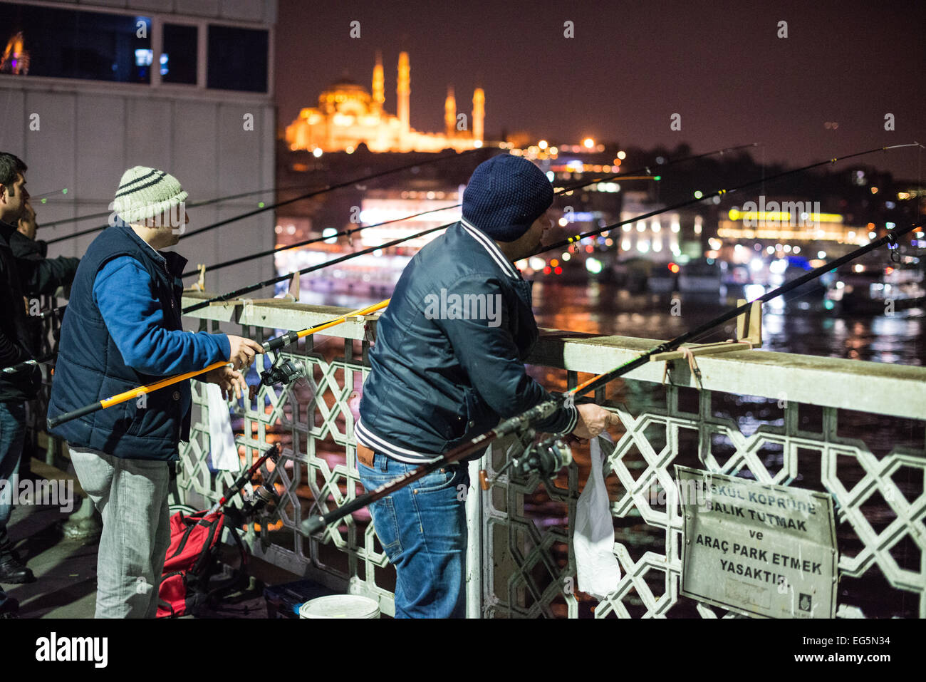 ISTANBUL, Turchia / Türkiye - i pescatori fiancheggiano il bordo del ponte di Galata con le loro linee sul lato del Corno d'Oro. Attraversando il Corno d'Oro e collegando Eminonu con Karakoy, il ponte Galata è un ponte a due livelli che gestisce il traffico stradale, del tram e pedonale al piano superiore con ristoranti e bar al livello sottostante. Foto Stock