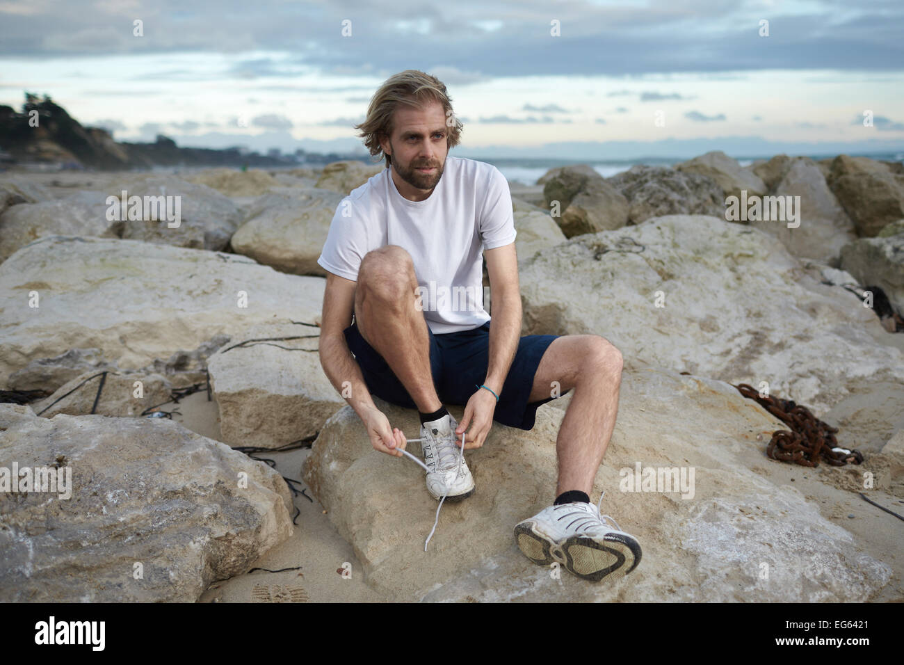 Un ritratto di stile di vita di un uomo nella sua 30's la legatura i suoi lacci da spiaggia prima di una corsa Foto Stock