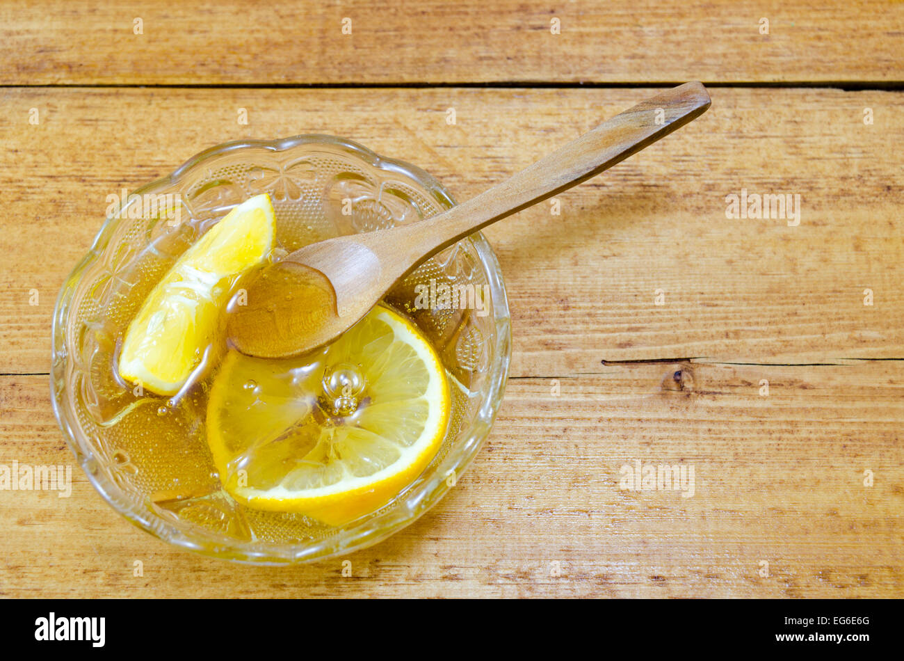 Lastra di vetro riempito con il miele e le fette di limone e un cucchiaio di legno Foto Stock