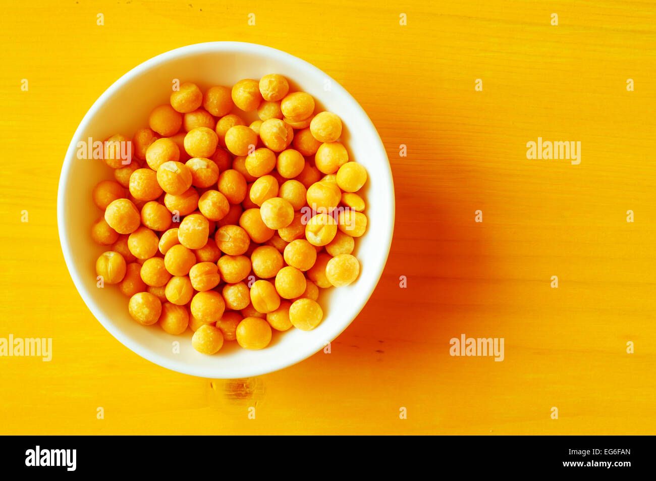 Solido giallo piselli secchi in una ciotola bianco su una tabella di colore giallo closeup. Vista superiore Foto Stock