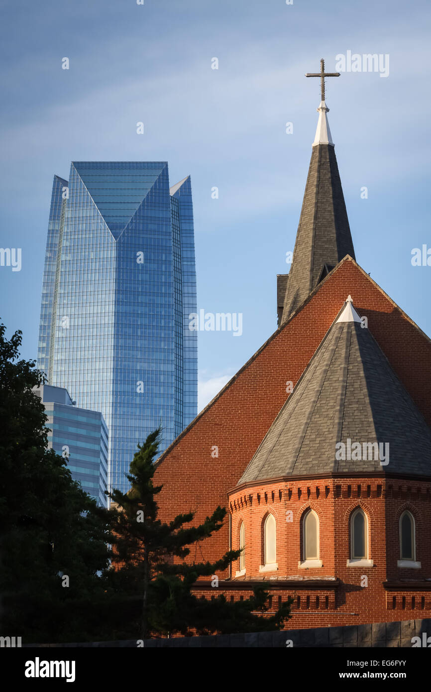 Visto dalla prospettiva di destra, il campanile e la croce di una piccola chiesa si erge contro l'edificio più alto della città. Foto Stock