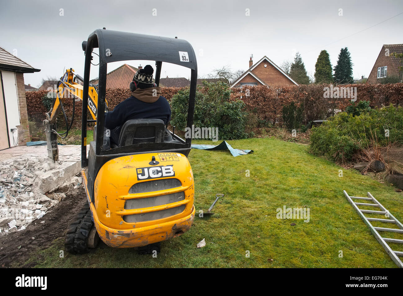 Lo scavo di vecchie basi basamenti su una estensione residenziale progetto utilizzando un pecker attaccato ad un escavatore compatto. Vista posteriore Foto Stock