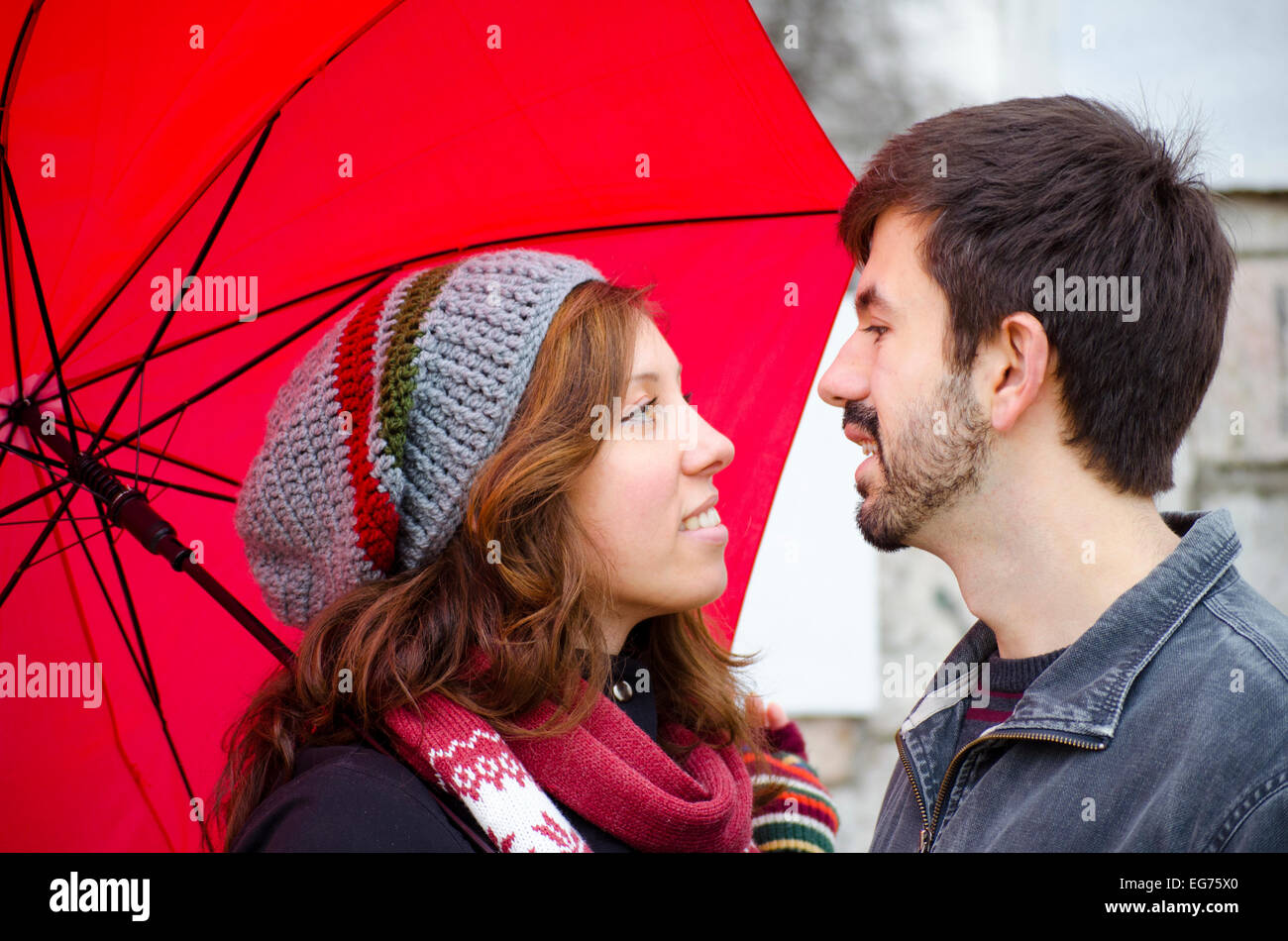 Ragazza caucasica e ragazzo lo scambio di sguardi amorevole sotto un ombrello rosso Foto Stock