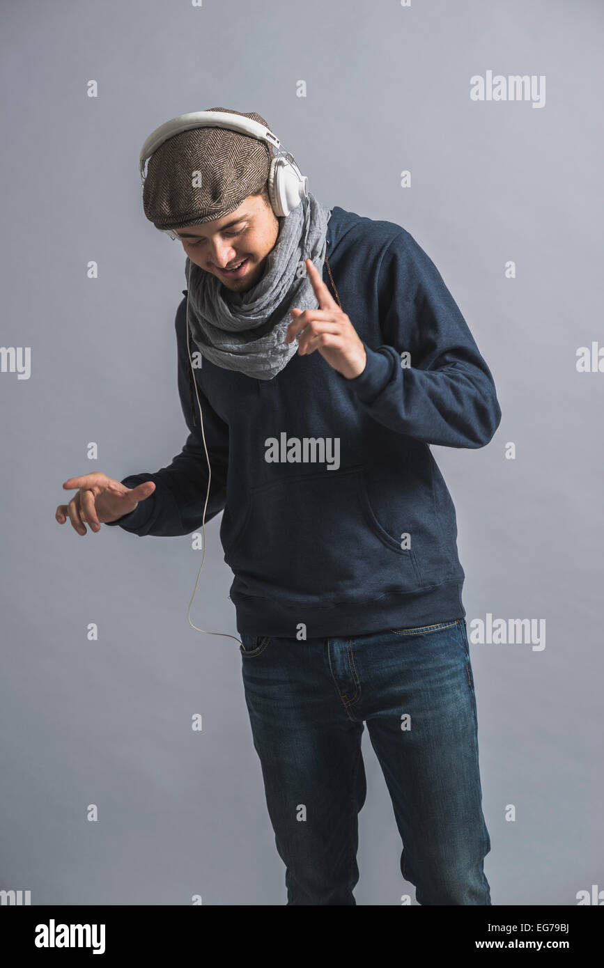 L'uomo con il cappuccio e le cuffie in piedi di fronte a uno sfondo grigio Foto Stock