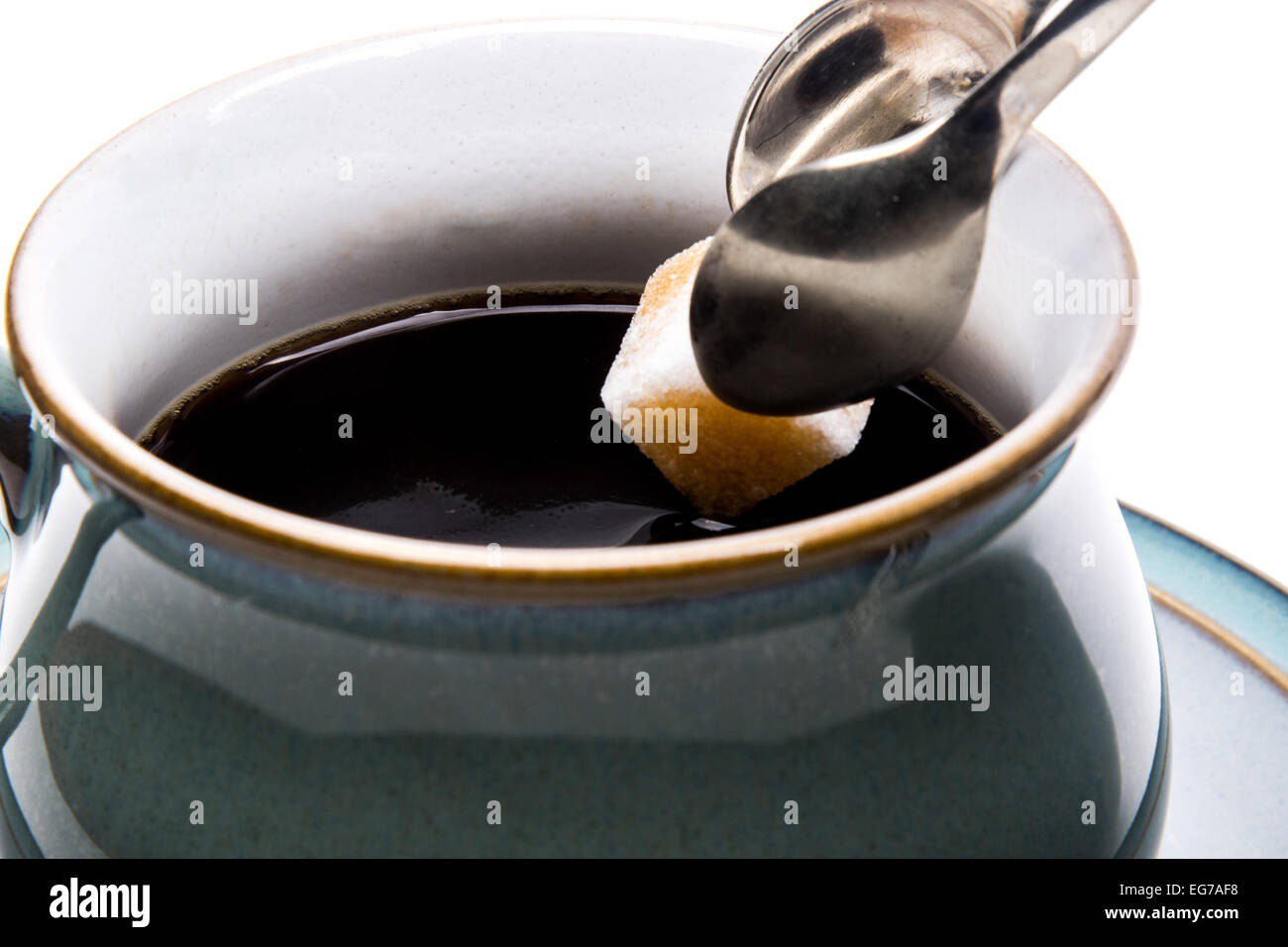 Un zucchero bianco cubo essendo immerso in una tazza di caffè nero mentre viene trattenuto da una coppia di pinze in argento Foto Stock