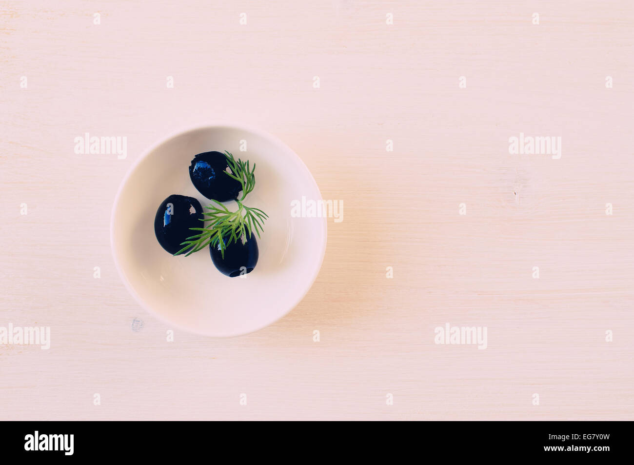 Olive nere tre pezzi in una tazza bianca su un tavolo bianco Foto Stock