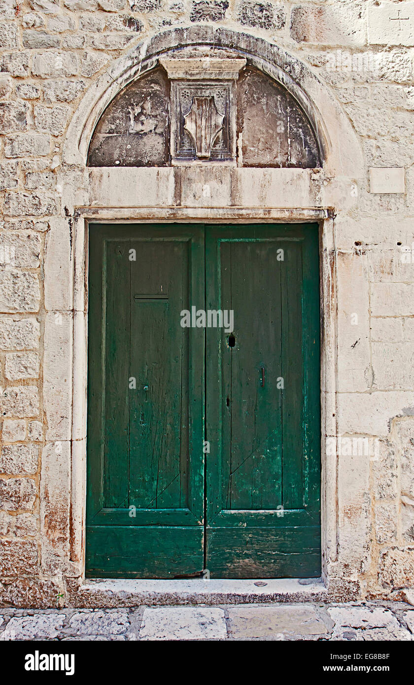 Antico portale con una verde porta di legno racchiusi in un bianco muro di pietra sormontata da un arco di marmo scolpito con scudo. Foto Stock