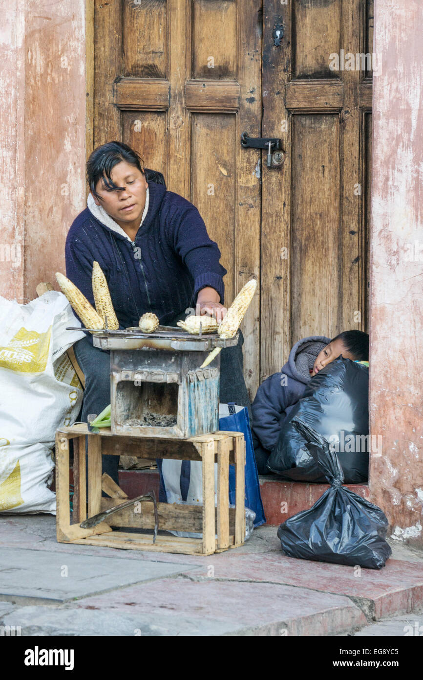 Donna indiana di mais per grigliare cibo di strada su stufa a carbone mentre suo figlio utilizza il sacco di orecchie come un cuscino San Christobal de las Casas Foto Stock