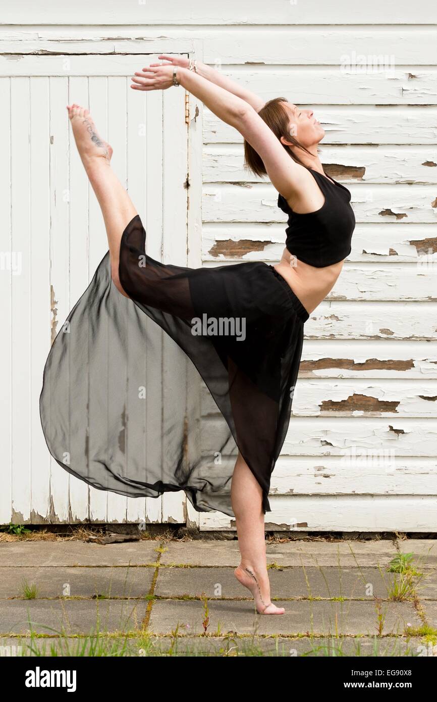 Ballerino femmina si riscalda al di fuori su lastre in calcestruzzo, di fronte a un capannone. Foto Stock