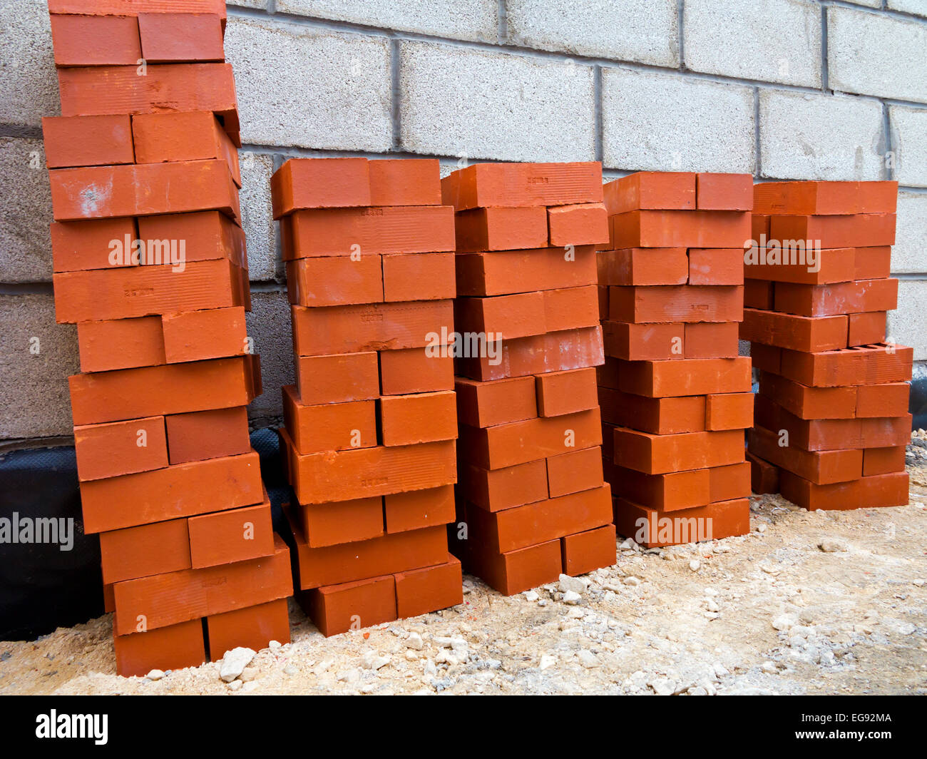 Rossi mattoni impilati pronti per essere posati su un sito di costruzione con pareti breezeblock visibile dietro Foto Stock