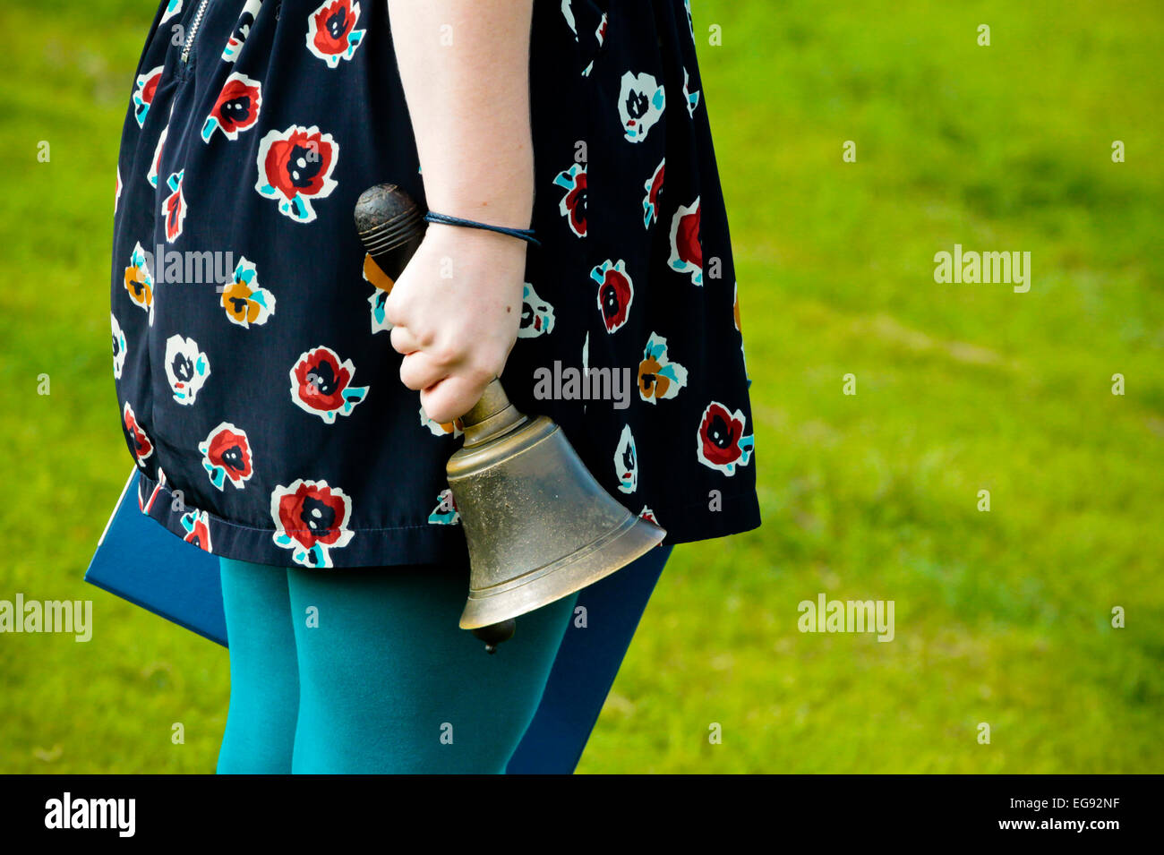 Femmina insegnante della scuola tenendo una mano tradizionale bell rung per contrassegnare la fine delle lezioni e il tempo di gioco in una scuola primaria nel Regno Unito Foto Stock