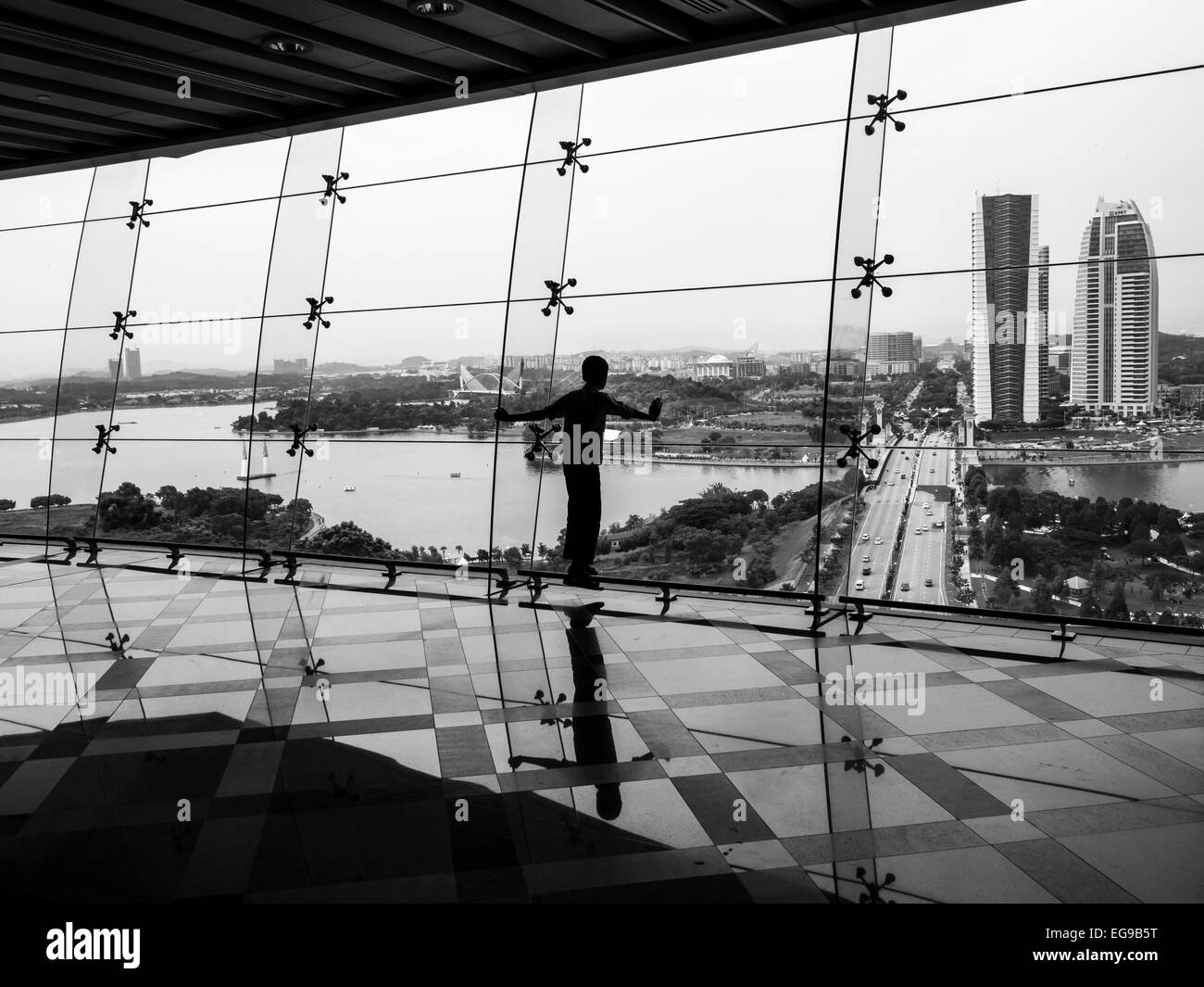 Silhouette di un ragazzo guardando un paesaggio urbano attraverso una parete di vetro Foto Stock