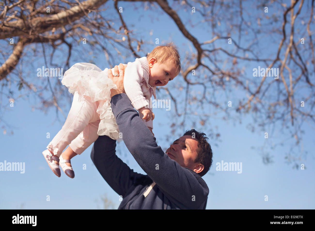 Padre holding aloft figlia sorridente (6-11 mesi) Foto Stock