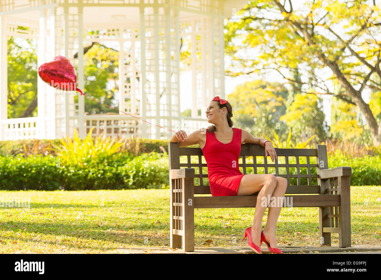 Donna con cuore rosso forma palloncino seduta su una panchina nel parco Foto Stock