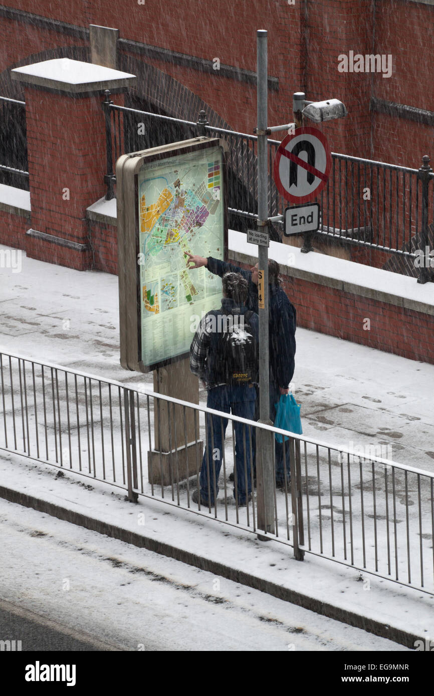 2 persone consultare una mappa, mentre si tenta di trovare la loro strada di casa sulla neve nel centro città di Manchester. Foto Stock