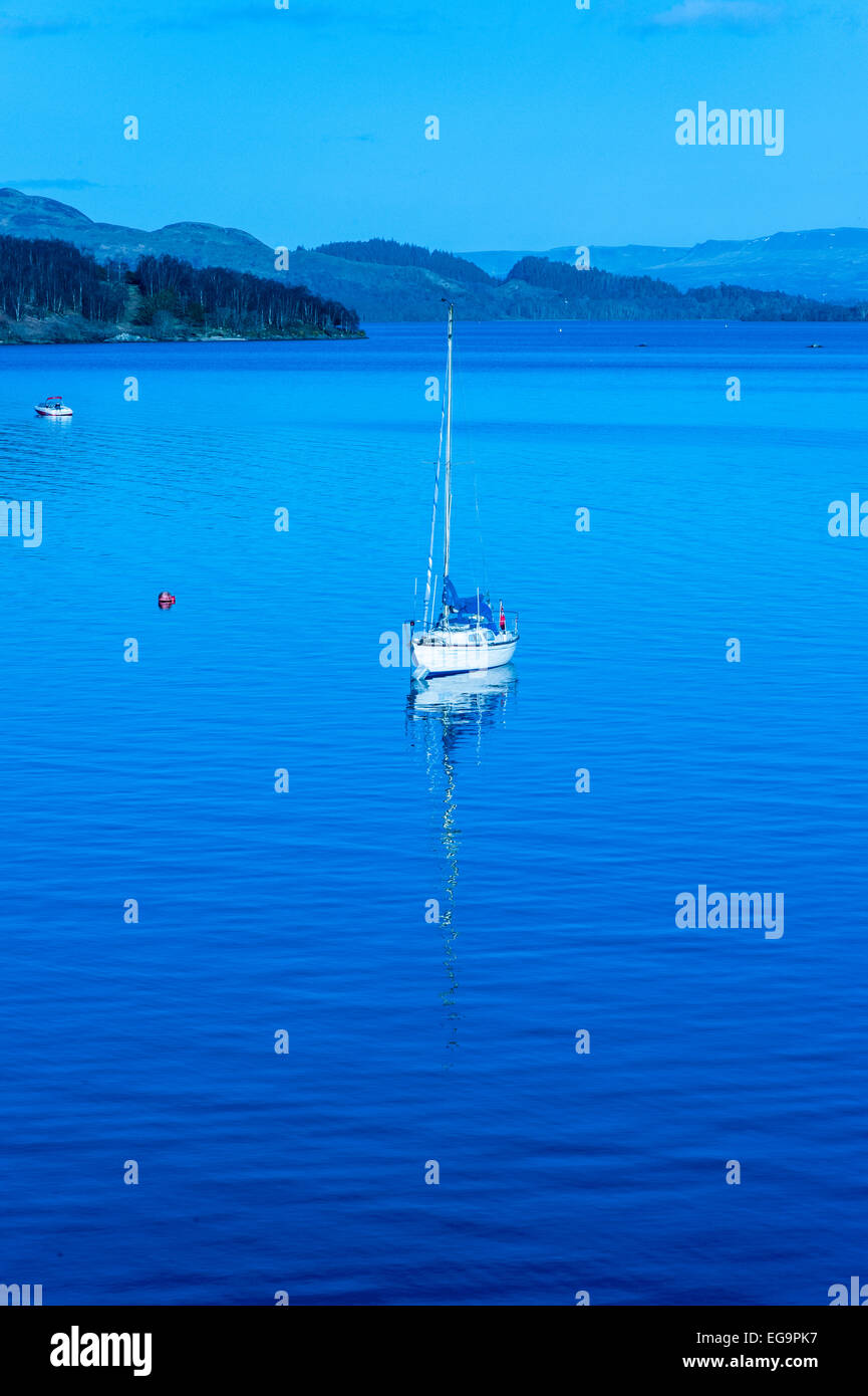 Unica barca a vela sul Loch Lomond al crepuscolo Foto Stock