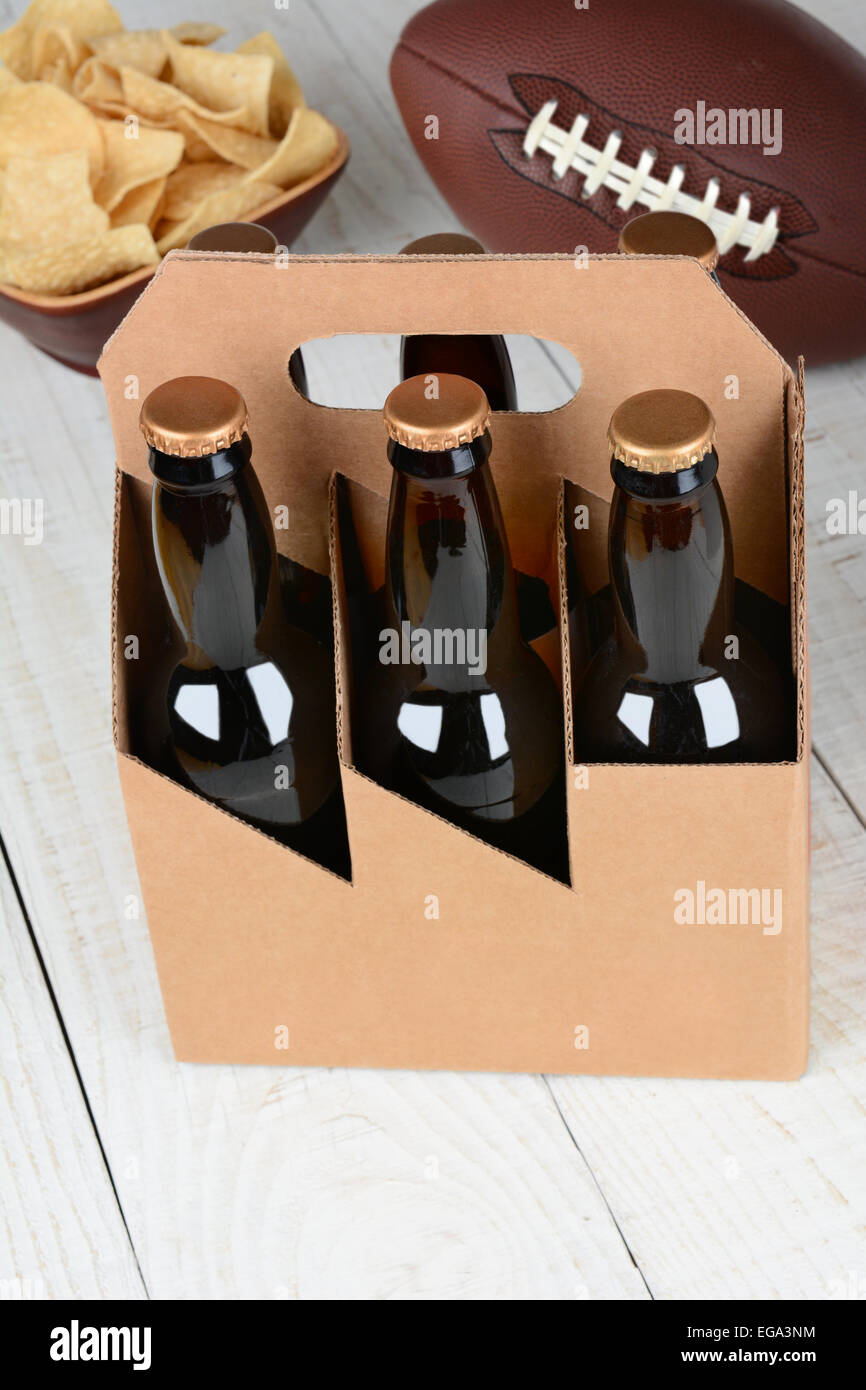Alta angolazione di un pacco di bottiglie di birra una ciotola di patatine e un american football. Formato verticale con il focus sulla birra Foto Stock