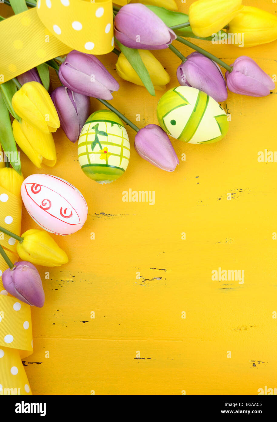 Felice Pasqua sfondo dipinto con le uova di Pasqua, giallo e viola i tulipani di seta e polka dot nastro su stile vintage rustico dis Foto Stock